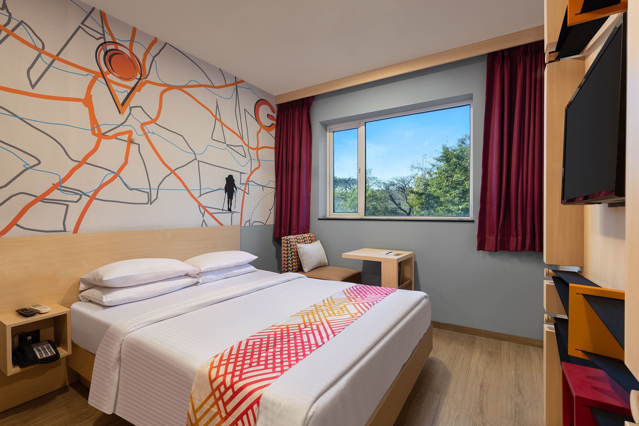 A hotel room with a large bed, a desk, a chair, a TV, and a window with curtains.