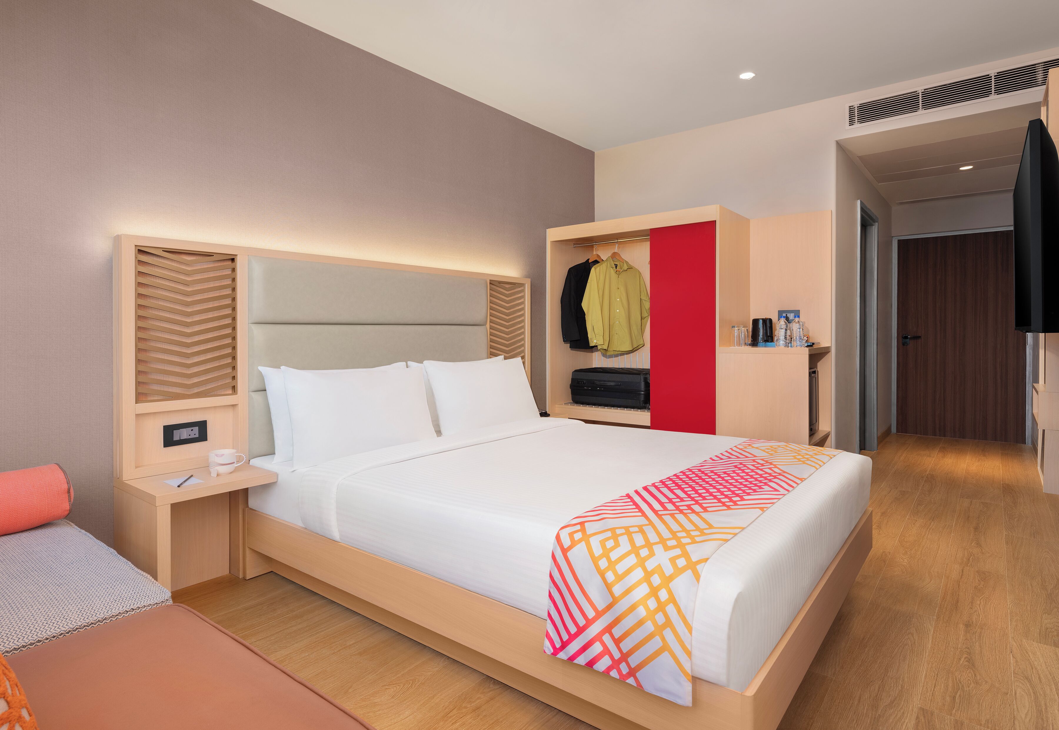 Una habitación de hotel moderna con una cama grande, una mesita de noche, un armario y un televisor.