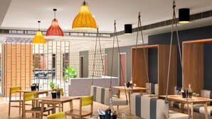 A modern restaurant with wooden tables and chairs, hanging pendant lights, and a view of the city through large windows. - Ginger Nagpur Airport Road (Nagpur)