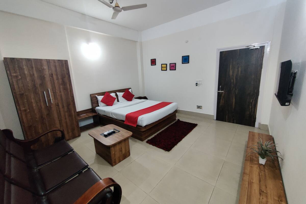 A bedroom with a bed, a desk, a chair, a wardrobe, a ceiling fan, a door, and a small plant.
