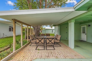 A covered patio with a brick floor, outdoor furniture, and a tree.