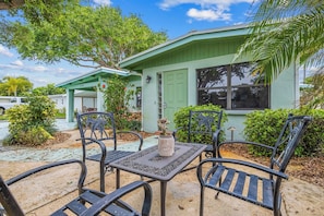 A house with a green exterior, a patio with metal chairs and a table, and a small garden area.