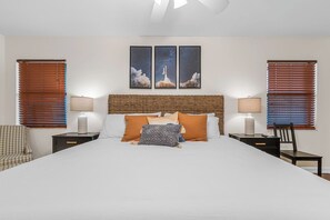A hotel room with a large bed, two nightstands, a wicker headboard, a wall-mounted lamp, and a framed space shuttle picture.