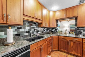 A kitchen with wooden cabinets, a granite countertop, a black sink, and a stainless steel range hood.