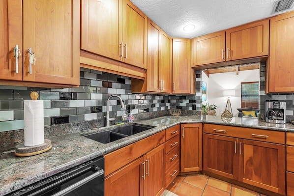 A kitchen with wooden cabinets, a granite countertop, a black sink, and a stainless steel range hood.