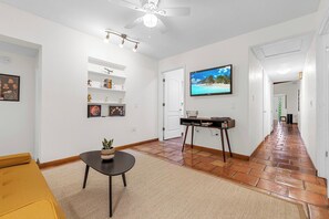 A hallway with a ceiling fan, a television mounted on the wall, and a tiled floor.