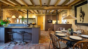 Una cocina rústica con vigas de madera a la vista, una isla central con taburetes de bar y un comedor con una mesa redonda para cuatro.