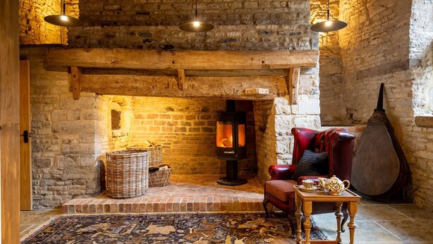 Una habitación acogedora con paredes de ladrillo visto, una chimenea, un sillón rojo, una mesa con tetera y un gran instrumento de cuerda.