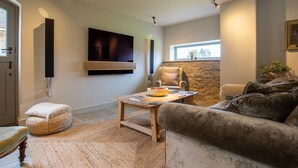 Una sala de estar moderna con una pared de piedra, una mesa de centro de madera, un sofá cómodo y un televisor de pantalla plana montado.