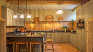 A kitchen with wooden cabinets, a central island with stools, pendant lighting, and a brick floor.