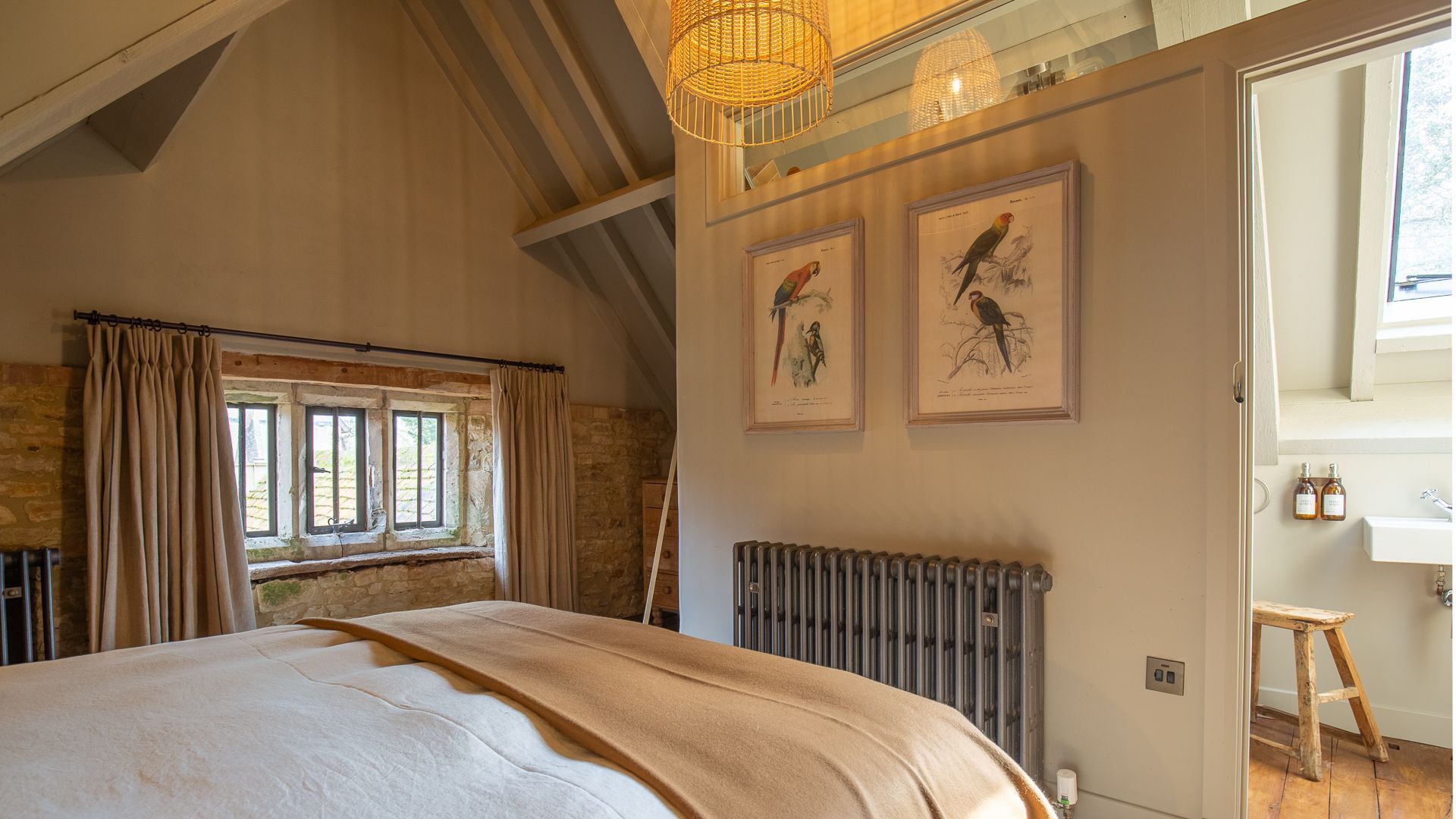 A bedroom with a large bed, a radiator, a window with curtains, and two framed bird illustrations on the wall.