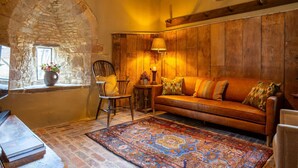 A cozy room with a stone wall, wooden paneling, a leather sofa, a patterned rug, and a wooden table with books.
