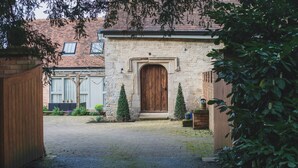 A stone building with a wooden door, a brick pathway, and a small garden with potted plants.