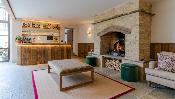 Una sala de estar acogedora con chimenea de piedra, una zona de bar de madera y un espacio de estar cómodo con un banco y un reposapiés.