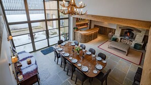 Un comedor con una gran mesa de madera dispuesta para seis personas, una chimenea y una zona de bar con pared de piedra.