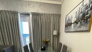Een moderne woonkamer met een glazen eettafel, grijze banken en een groot abstract schilderij aan de muur.