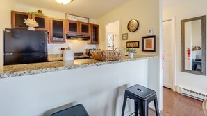 A kitchen with a black refrigerator, wooden cabinets, a granite countertop, a woven basket, and a clock on the wall. - Beech Mtn Studio < 1 Mi to Skiing: Bring Your Pet! (Beech Mountain)