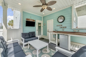 A covered outdoor seating area with a ceiling fan, a clock, and a sign that reads "CRAB SHACK BY THE SEA".