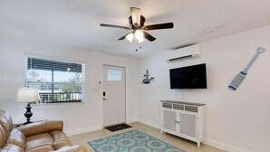 A living room with a ceiling fan, a TV mounted on the wall, a cabinet, and a patterned rug.