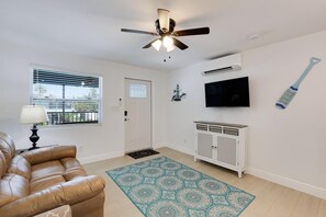 A living room with a ceiling fan, a TV mounted on the wall, a cabinet, and a patterned rug.