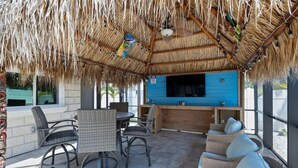 An outdoor seating area with wicker furniture, a blue counter, and a thatched roof.