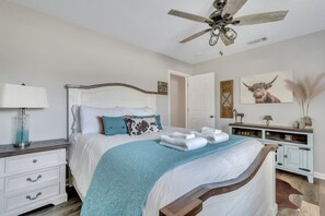 A bedroom with a bed, nightstands, a ceiling fan, a dresser, and a door.