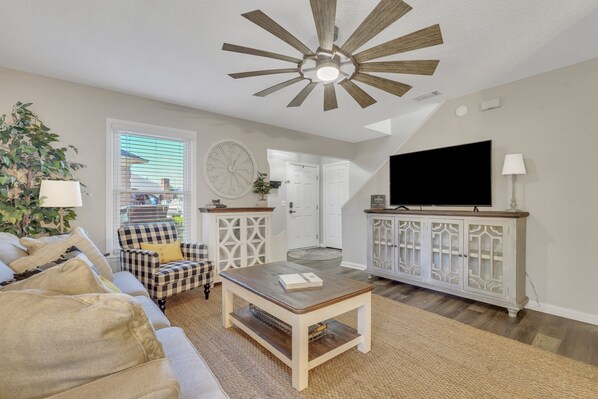 A living room with a ceiling fan, a television, a checkered armchair, and a coffee table.