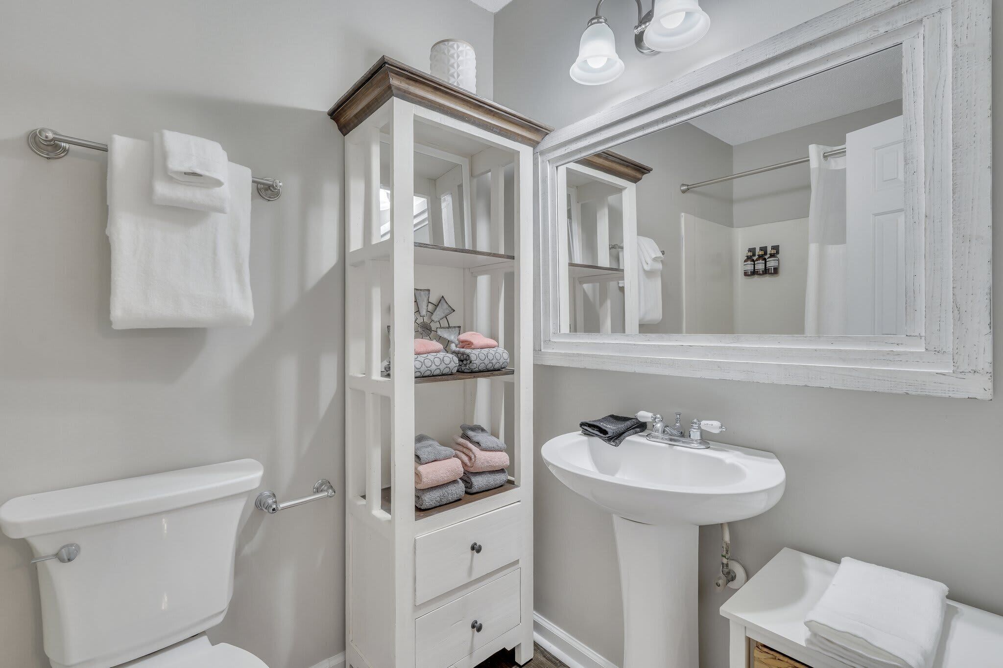 A bathroom with a toilet, a white cabinet with shelves, a sink, and a mirror.