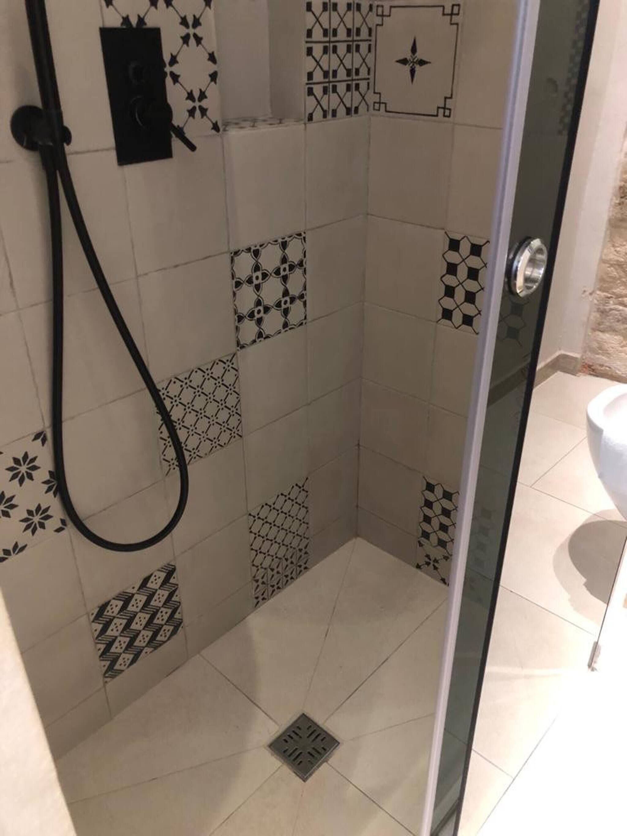 Ducha con puerta de vidrio, paredes cubiertas de azulejos con patrones geométricos y desagüe a la vista.