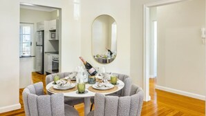 A dining area with a round table set for four, a mirror on the wall, and a kitchen in the background. - Riverview casa/ walk to Mater & children hospital (South Brisbane)