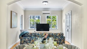 A dining area with a round table set for six, a floral sofa, and a television in the background. - Riverview casa/ walk to Mater & children hospital (South Brisbane)