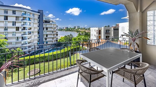 Un balcón con mesa y sillas, con vistas a una piscina y edificios.