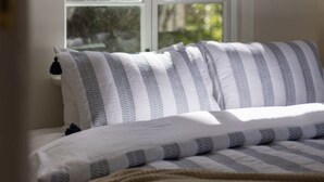 Un dormitorio con un ventanal grande, una cama con ropa de cama a rayas y vistas a árboles desde el exterior.
