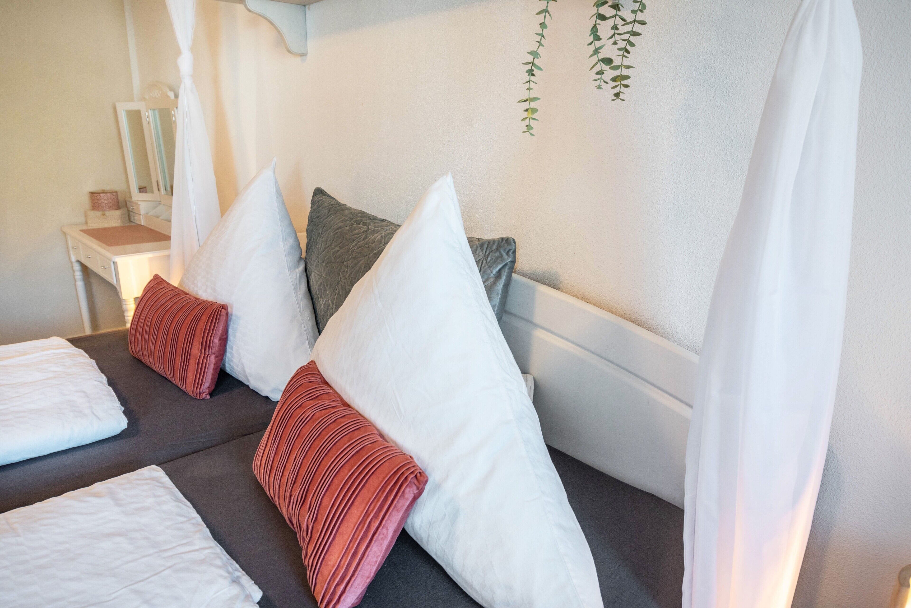 Een slaapkamer met een bed, kussens, een nachtkastje en een spiegel.