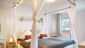 Una cama con dosel, una mesita de noche con lámpara y una silla en una habitación con ventana y radiador.