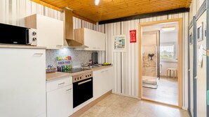 A kitchen with white cabinets, a black oven, and a microwave. There is a wooden ceiling and a door leading to a balcony. - Apartment 'Djuren' with Private Terrace, Shared Garden, and Wi-Fi (Niedersachsen - Emden)