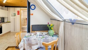 A dining area with a table set for four, a clock on the wall, and a view through a window. - Apartment 'Djuren' with Private Terrace, Shared Garden, and Wi-Fi (Niedersachsen - Emden)