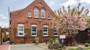 A red brick building with a triangular roof, a clock, and a sign with a name and address. - Apartment 'Djuren' with Private Terrace, Shared Garden, and Wi-Fi (Niedersachsen - Emden)