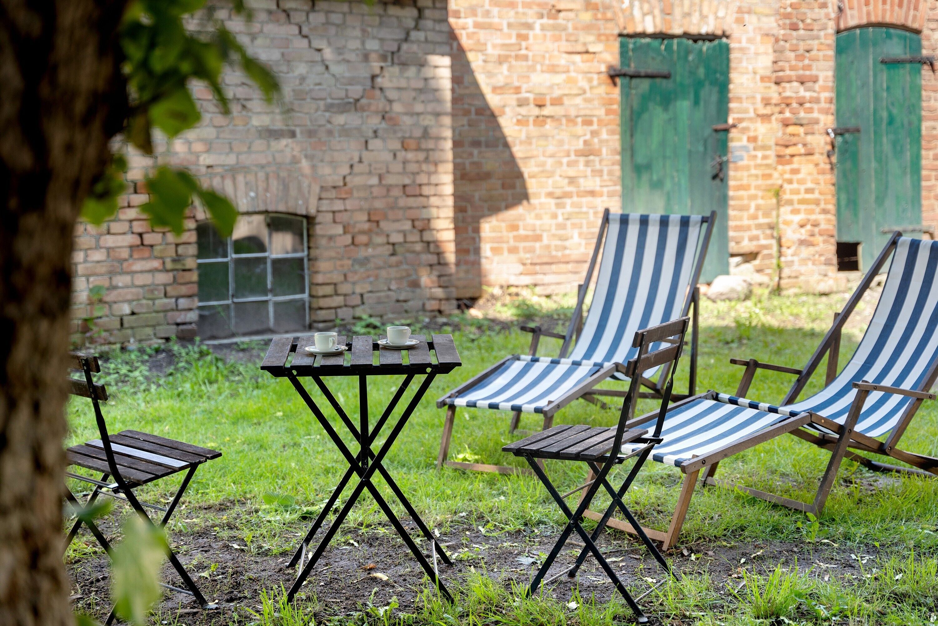 Un jardin avec une table et quatre chaises à rayures, un mur de briques et un arbre.