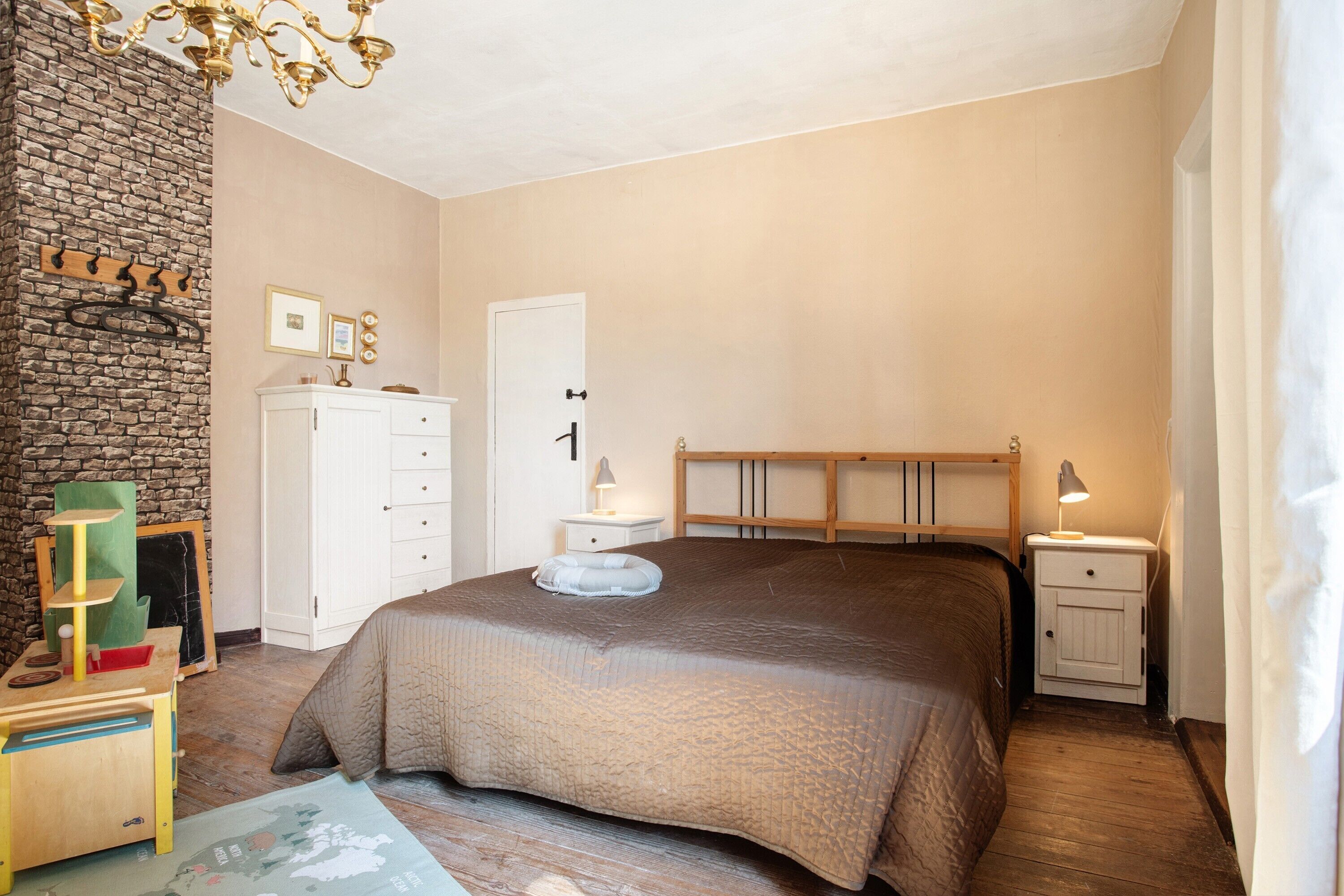 Ein Schlafzimmer mit einem großen Bett, einem hölzernen Kopfteil, einem weißen Kleiderschrank, einem kleinen Nachttisch und einem an der Wand befestigten Regal.