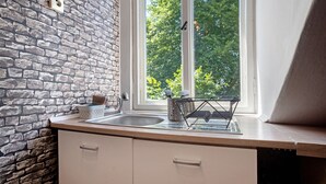 A kitchen with a stone wall, a window with a view of trees, and a dish rack on the counter.