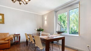 A dining area with a wooden table, chairs, a vase with flowers, and a window with a view of trees.