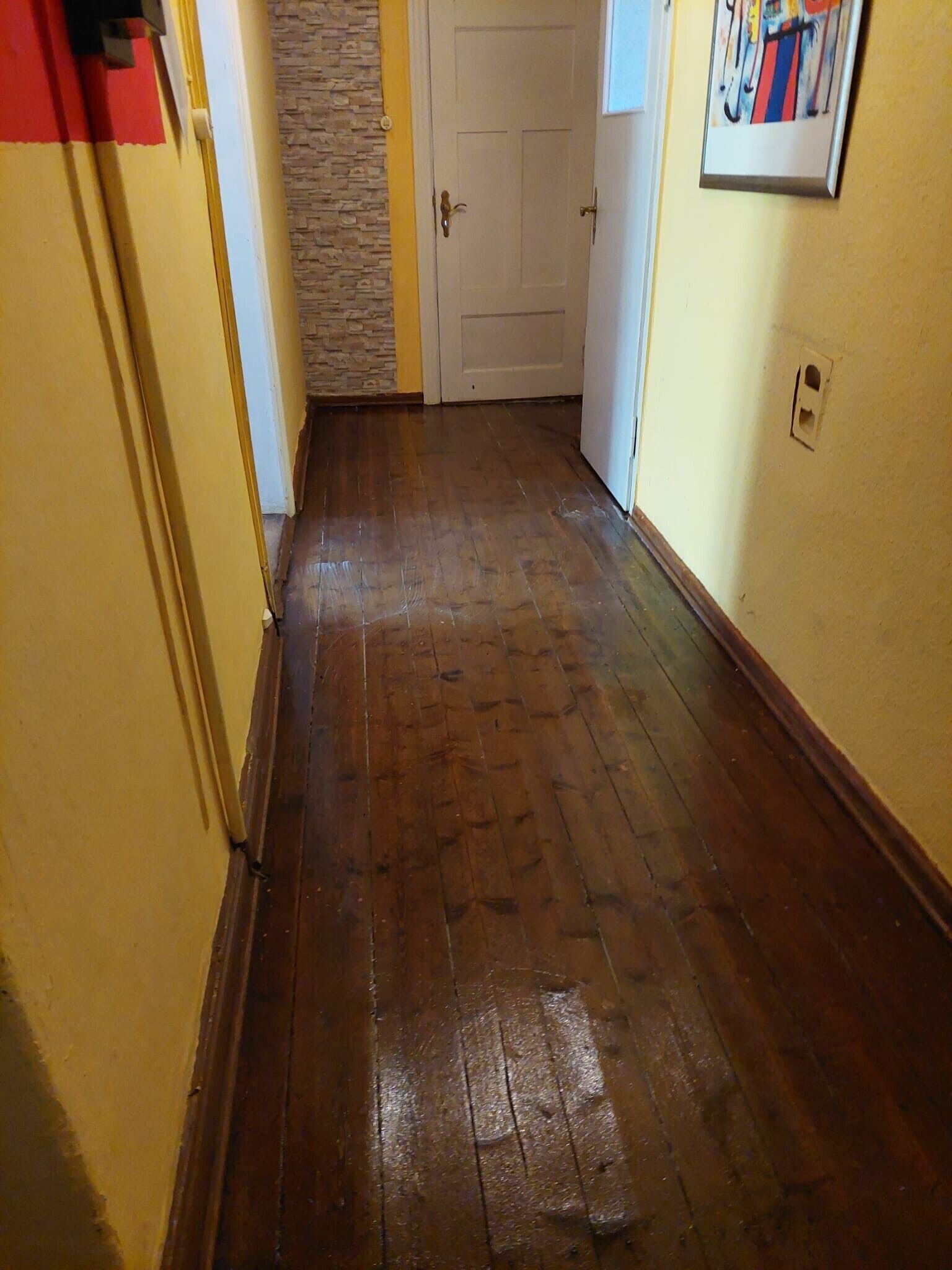 A hallway with wooden flooring, a door, and a wall-mounted light switch.