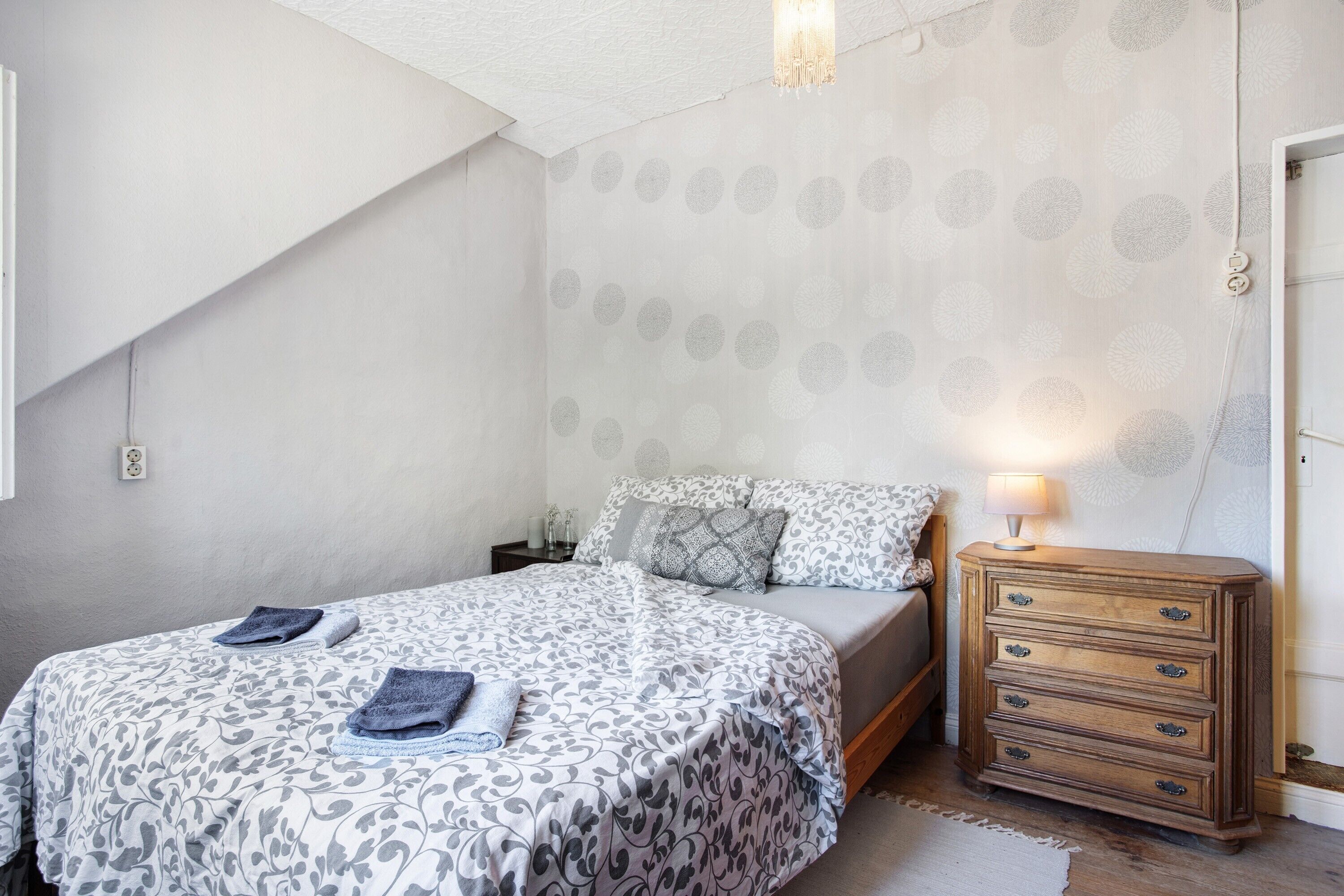 A bedroom with a bed, a dresser, a lamp, and a patterned wall.