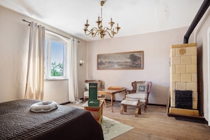 A room with a bed, a chandelier, a painting, a fireplace, and a window with curtains.