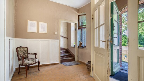 A room with a chair, a staircase, and a door leading outside.