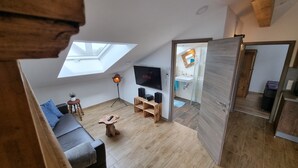 Habitación tipo loft con tragaluces, televisor, sofá y una pequeña mesa de madera.