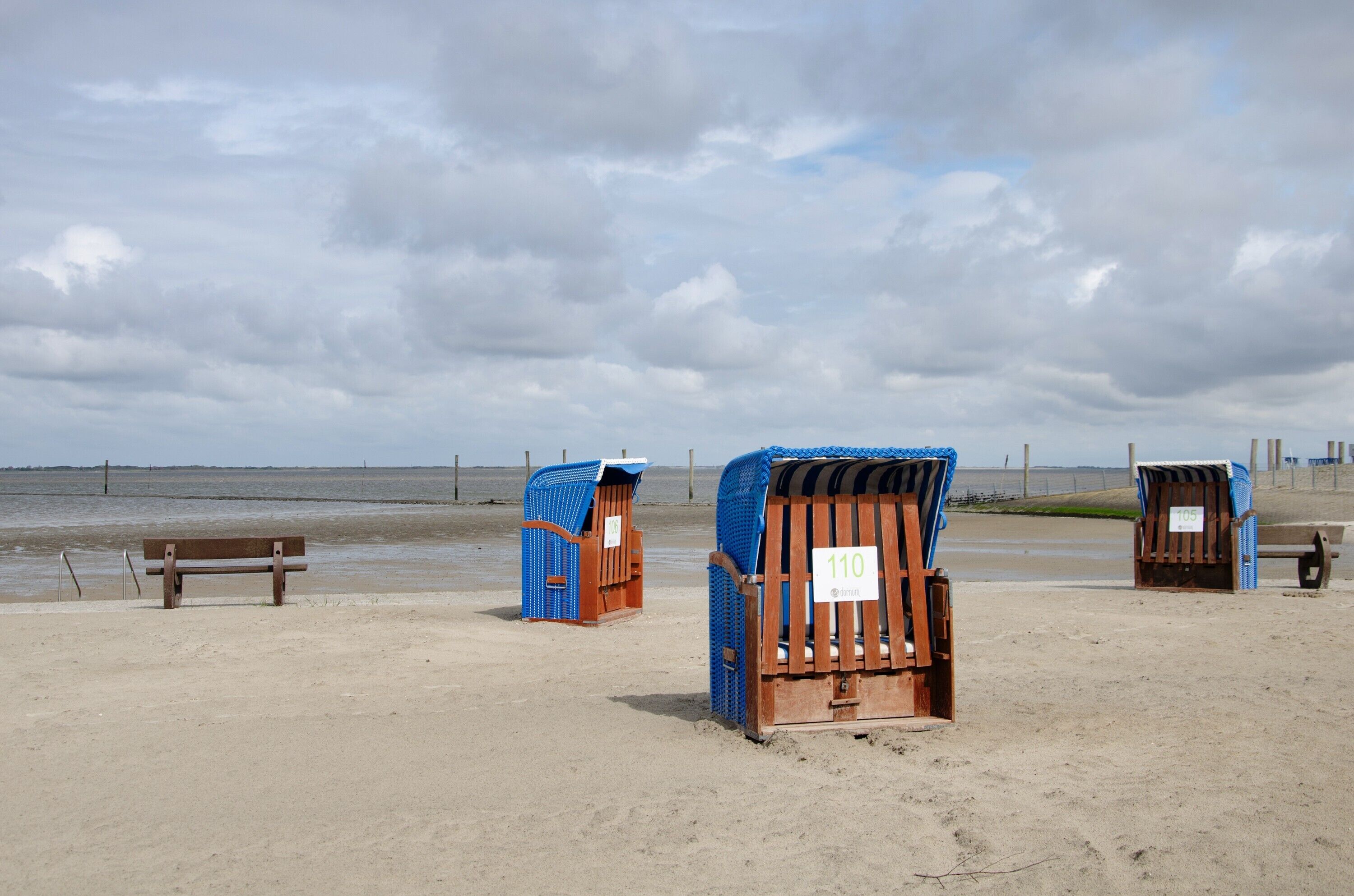 A beach with a wooden bench and three beach huts.