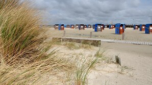 A row of beach huts with a sandy beach and dunes in the foreground. - Holiday Apartment 'Ferienhaus Deichblick Nessmersiel' with Private Terrace, Garden & Wi-Fi (Dornum)