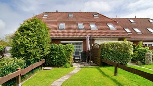 A two-story house with a tiled roof, a front garden, and a pathway leading to the entrance. - Holiday Apartment 'Ferienhaus Deichblick Nessmersiel' with Private Terrace, Garden & Wi-Fi (Dornum)